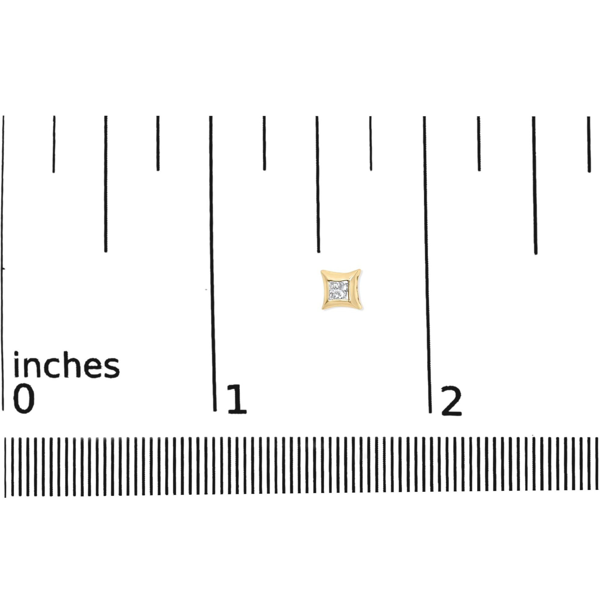 Close-up of a yellow metal square-shaped earring with a white gemstone in the center, shown on a ruler for size reference.