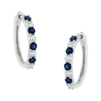 Pair of white metal hoop earrings with alternating round white and blue gemstones in prong settings, shown at a slight angle.