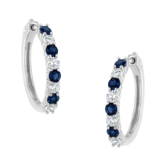 Pair of white metal hoop earrings with alternating round white and blue gemstones in prong settings, shown at a slight angle.