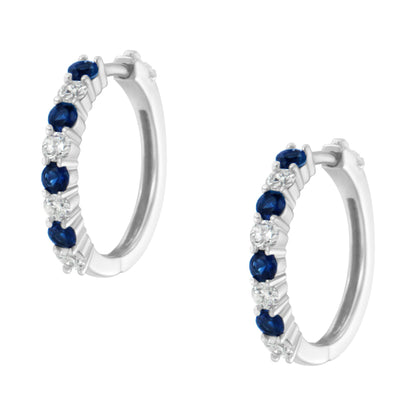 Pair of white metal hoop earrings with alternating round white and blue gemstones in prong settings, shown at a slight angle.