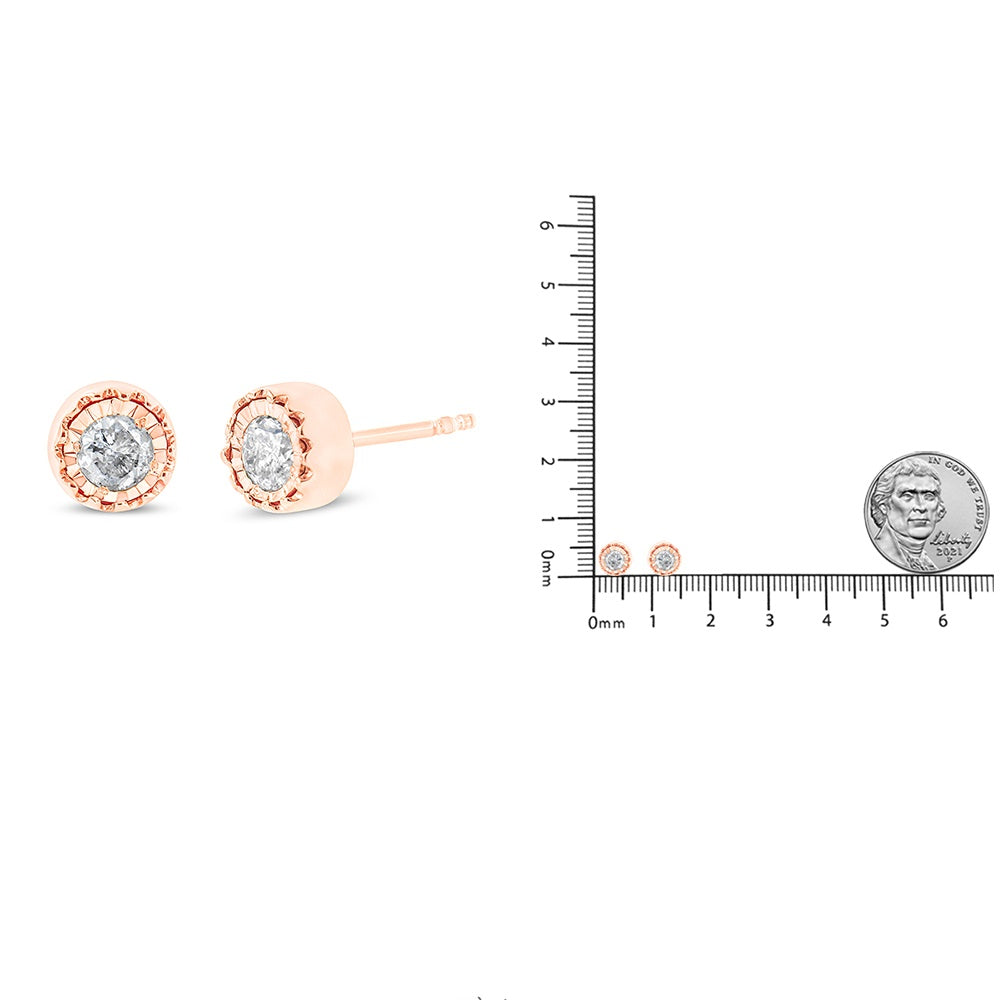 Rose-colored stud earrings with round white gemstones in miracle setting shown from the side and front, alongside a ruler and coin for size reference.