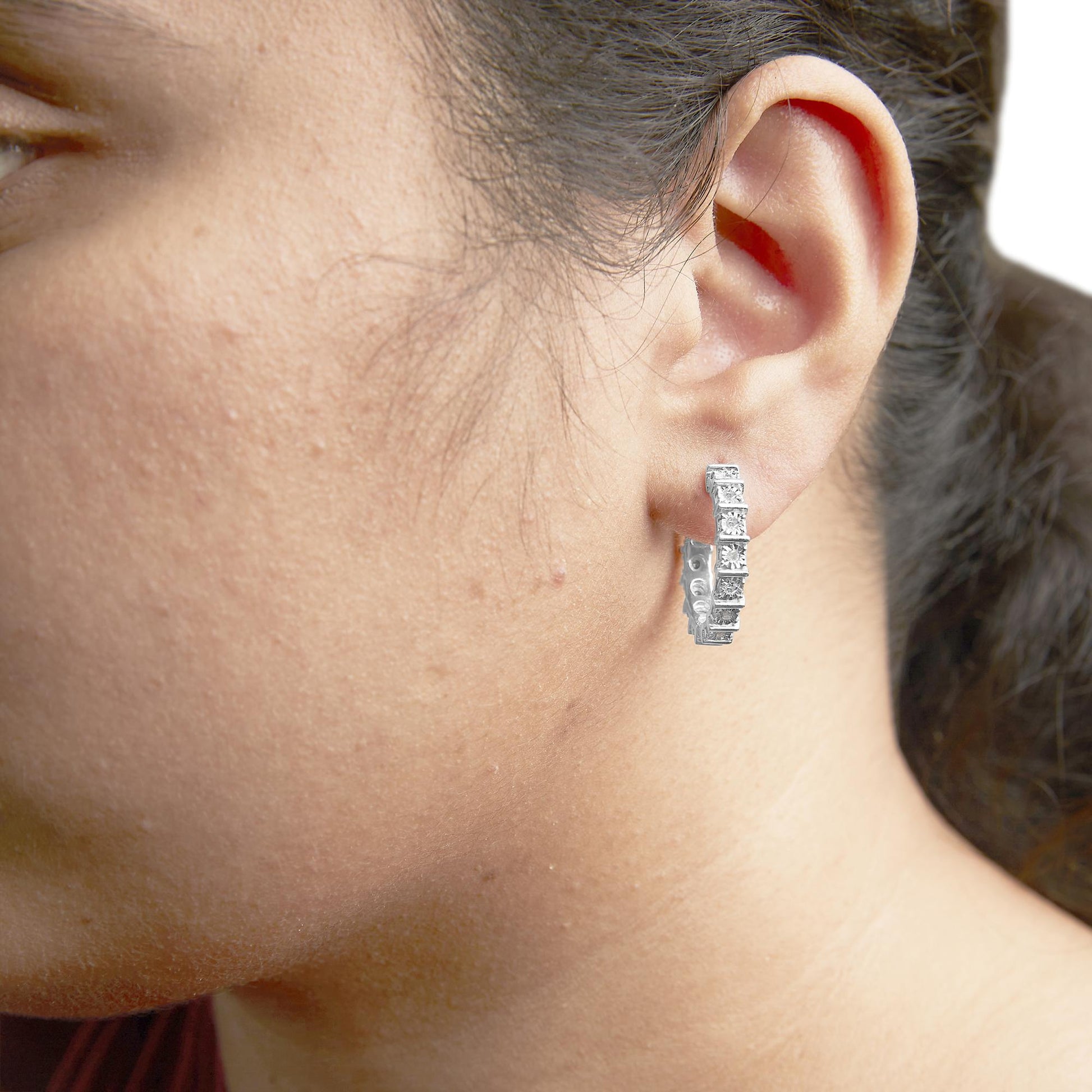 Close-up side view of a white metal hoop earring with round white gemstones in a miracle setting, worn on a model.