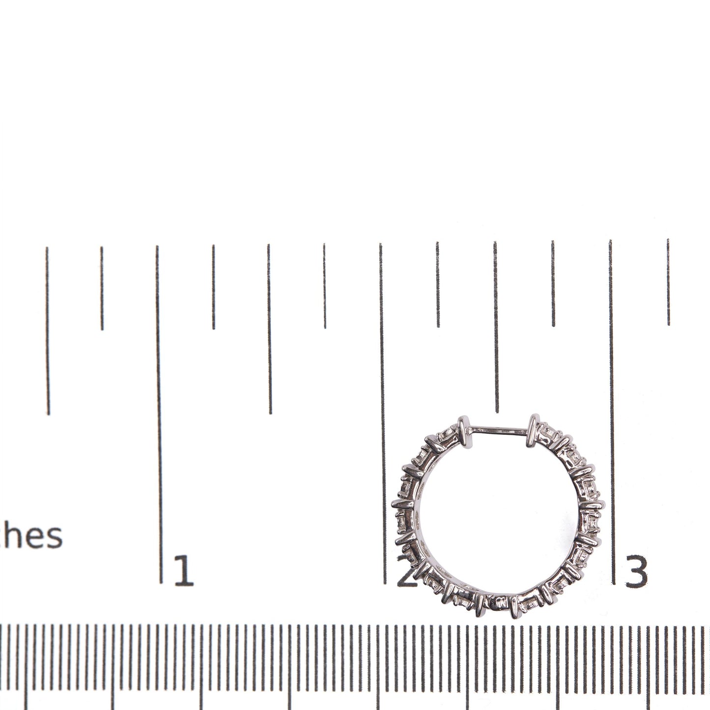 White metal hoop earring with round white gemstones in miracle setting, photographed flat on a ruler for size reference.