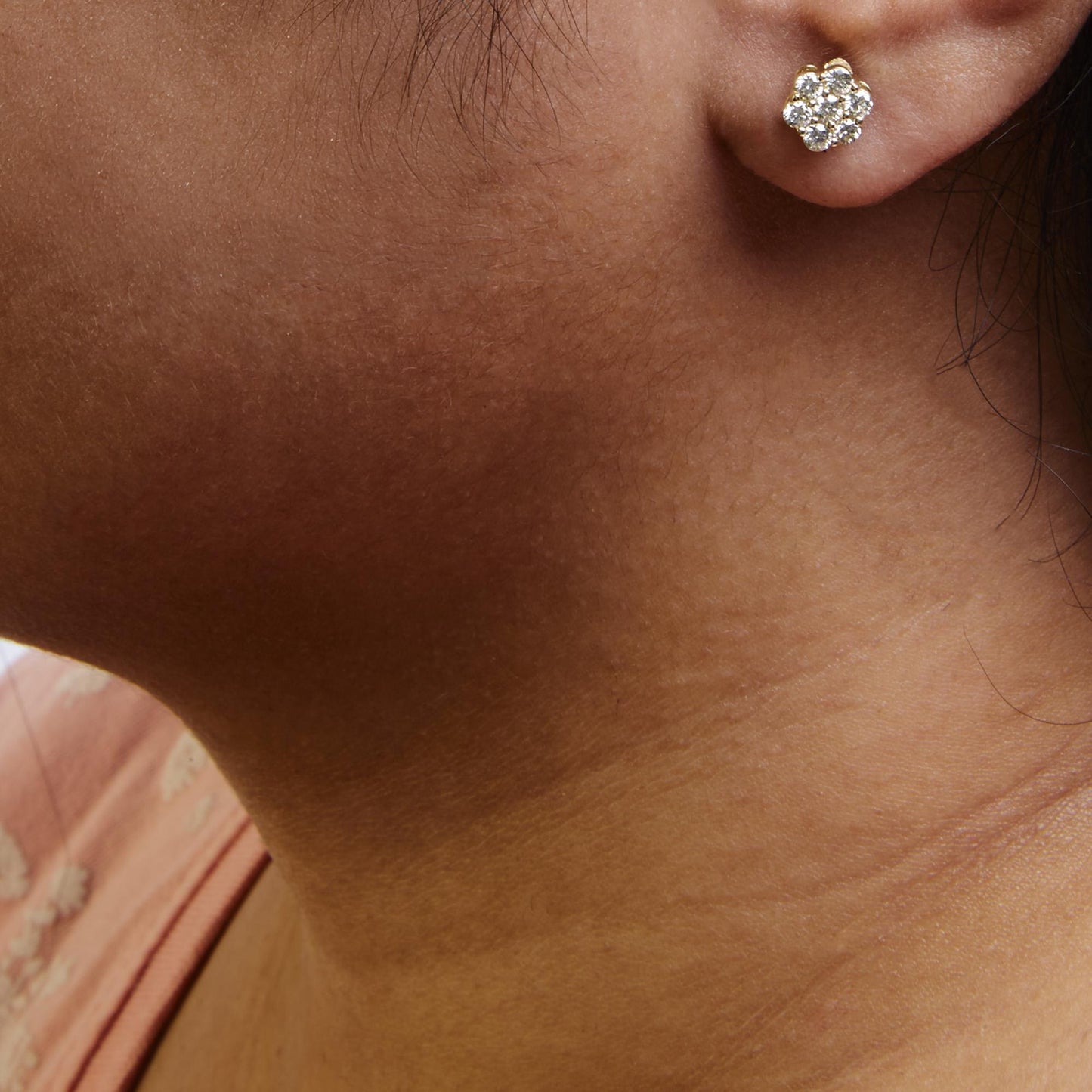 Close-up side view of a yellow metal earring with round white gemstones in a cluster prong setting worn on a model's ear.