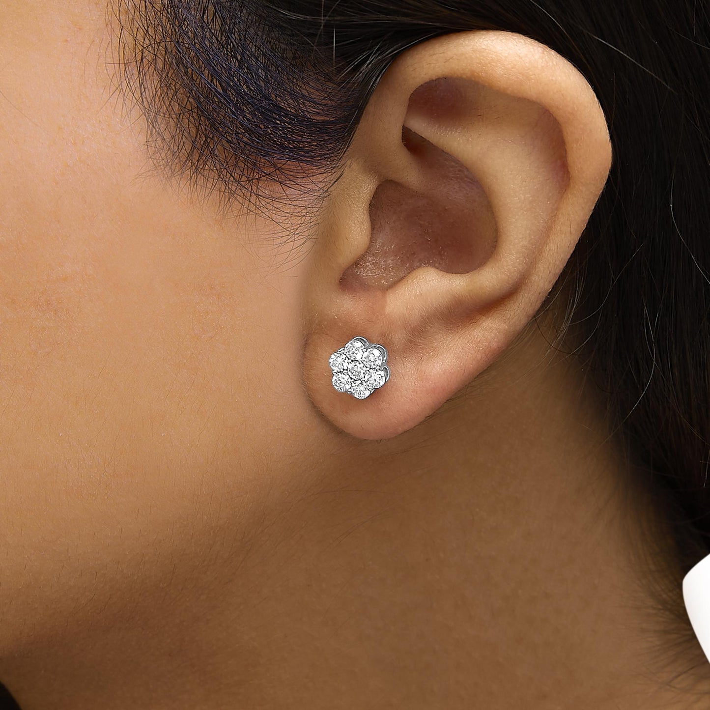 Close-up side view of a white metal flower-shaped stud earring with round white gemstones in prong settings, worn on a model's ear.