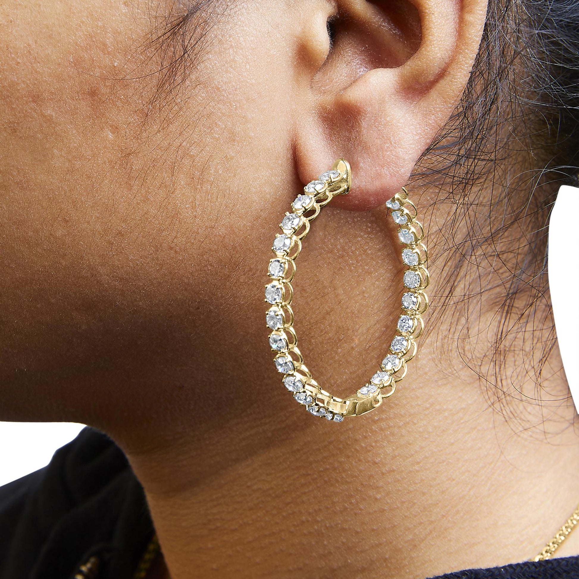 Close-up side view of a yellow metal hoop earring with round white gemstones in prong settings, shown worn on a model.