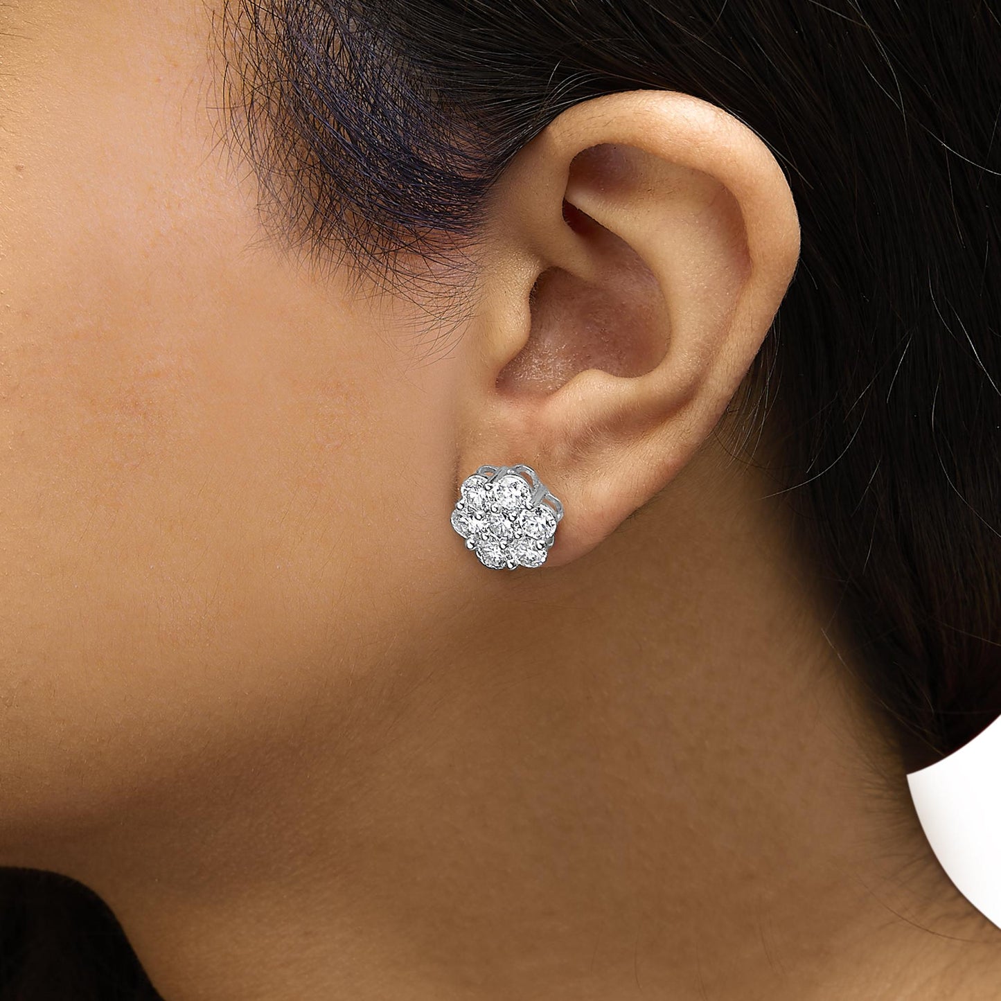 Close-up side view of a white metal cluster earring with round white gemstones in shared prong settings, worn on a model's ear.