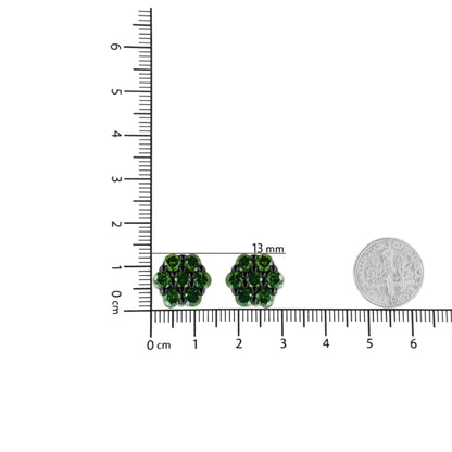 Top down view of white metal earrings with round green gemstones in prong settings placed on a ruler and scale for size reference.