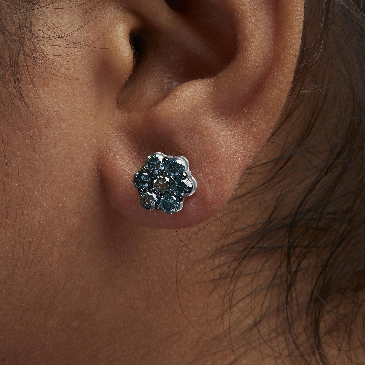 Close-up side view of a white metal flower-shaped earring with round white gemstones in prong settings, worn on a model's ear.