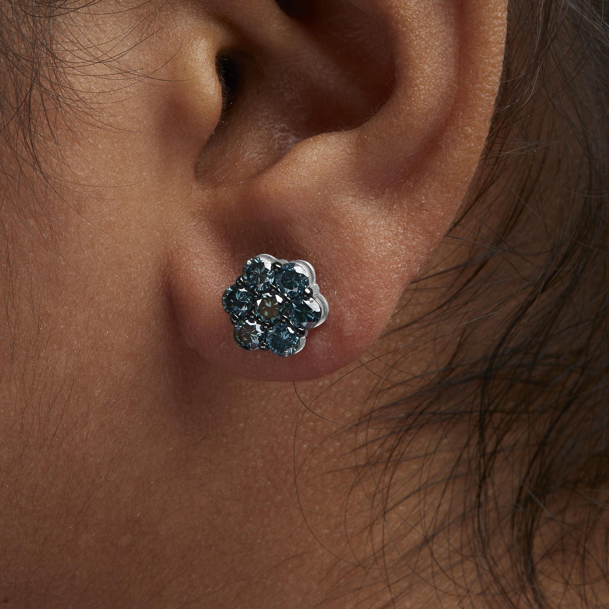 Close-up side view of a white metal flower-shaped earring with round white gemstones in prong settings, worn on a model's ear.