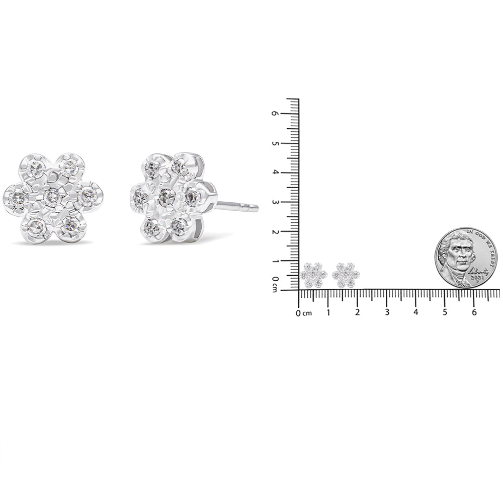 Close-up front and side view of white metal flower-shaped stud earrings with round prong-set white gemstones, shown next to a ruler and coin for size reference.