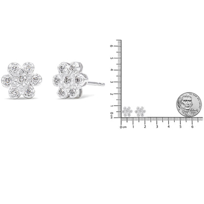 Close-up front and side view of white metal flower-shaped stud earrings with round prong-set white gemstones, shown next to a ruler and coin for size reference.