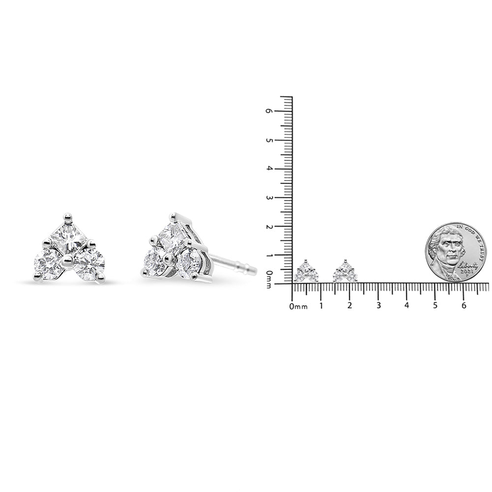 Pair of white metal earrings with a triangular arrangement of one princess-cut and three round-cut white gemstones, shown at a front and side angle next to a ruler and coin for size reference.