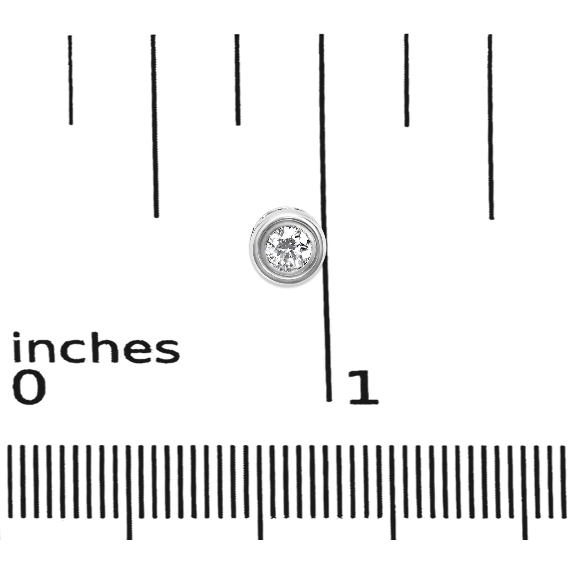 Close-up top view of a single white metal round bezel-set earring with a white gemstone, placed on a ruler for size reference.