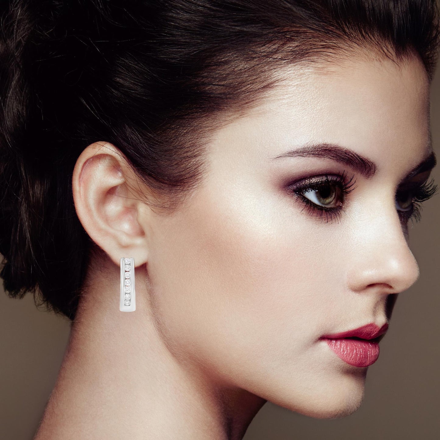 Close-up side view of a woman wearing white metal earrings with a vertical channel setting of round white gemstones.