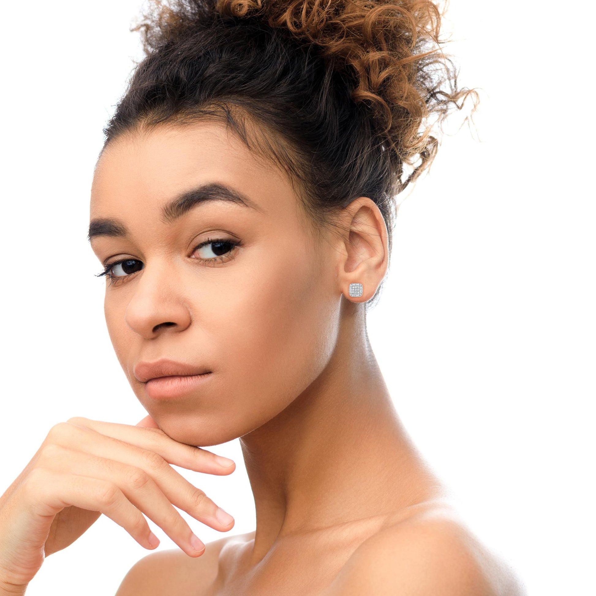 Close-up side angle of a model wearing white metal stud earrings featuring princess shape white gemstones in an invisible setting surrounded by baguette shape white gemstones in a prong setting.
