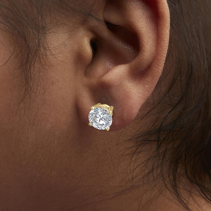 Close-up side view of a model's ear wearing a yellow metal stud earring with a round white gemstone in a four-prong setting.