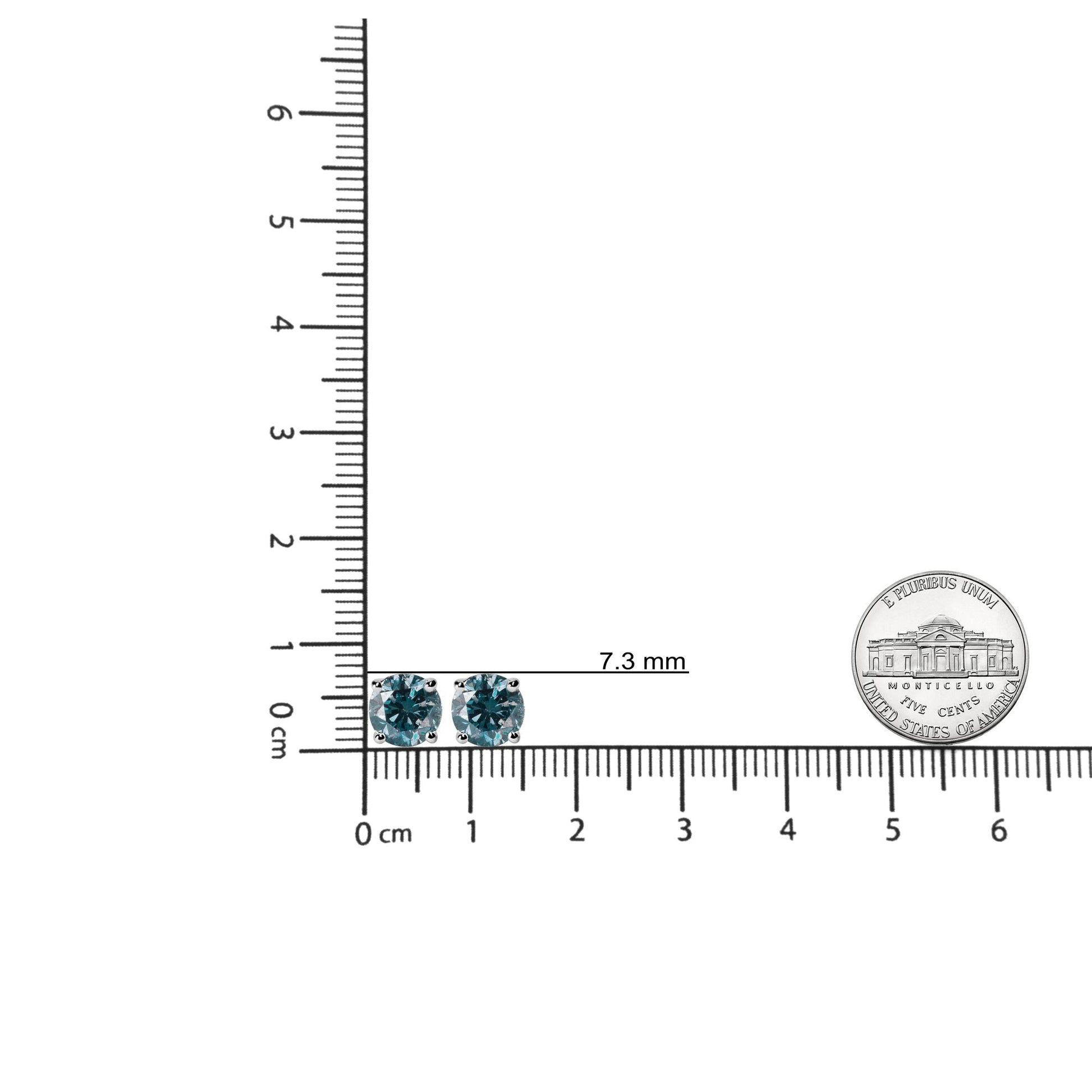Top-down view of white metal stud earrings with round blue gemstones in 4-prong settings, placed on a ruler for size reference.