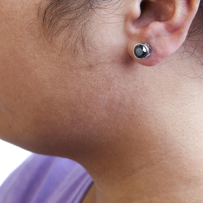 Close-up side angle of a model wearing white metal round bezel-set black gemstone stud earrings.