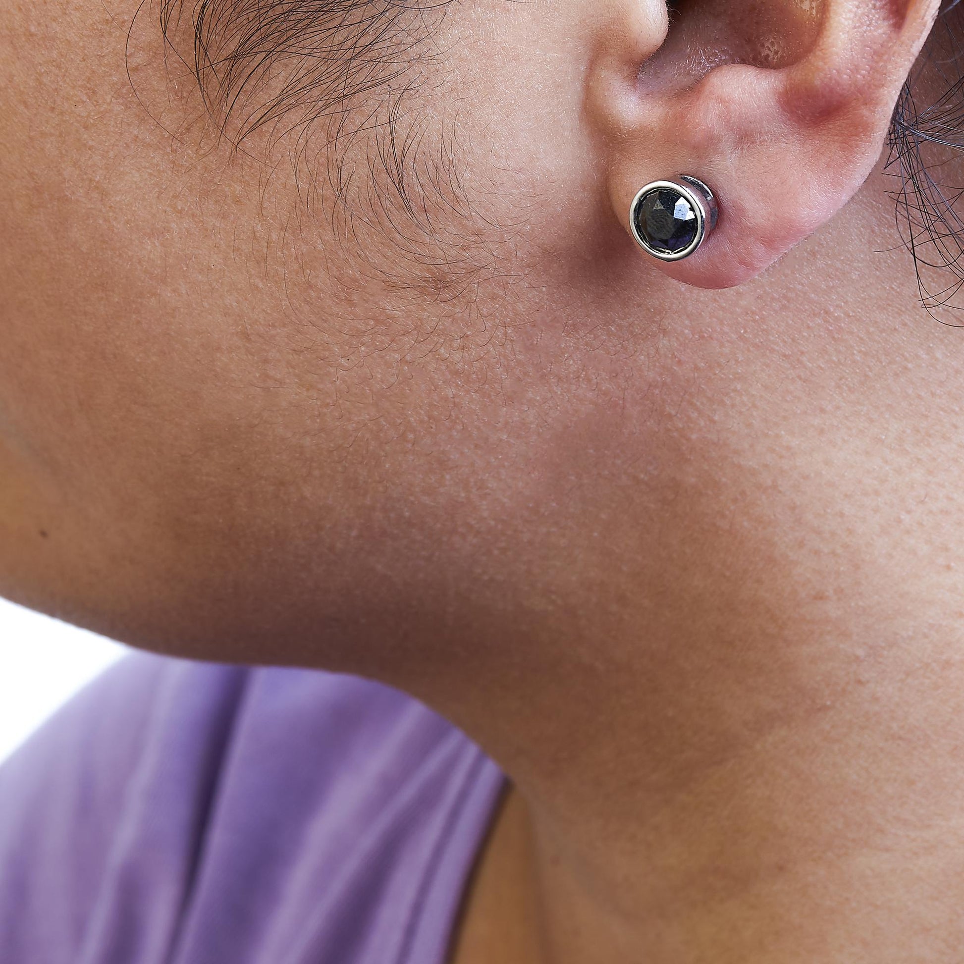 Close-up side view of a white metal stud earring with a round black gemstone in bezel setting, worn on a model's ear.