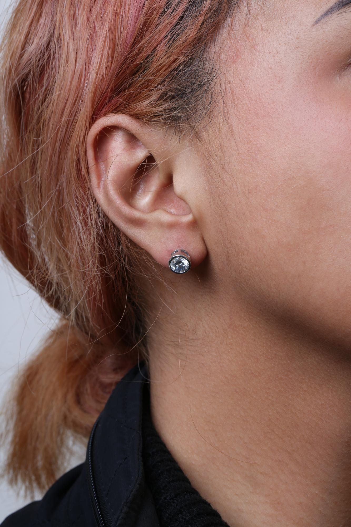 Close-up side view of a model wearing a white metal stud earring with a round white gemstone in bezel setting.