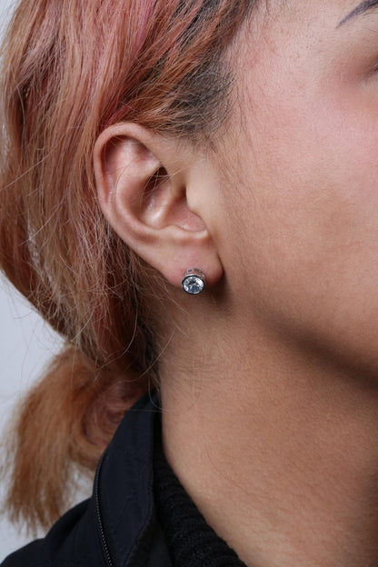 Close-up side view of a model wearing a white metal stud earring with a round white gemstone in bezel setting.
