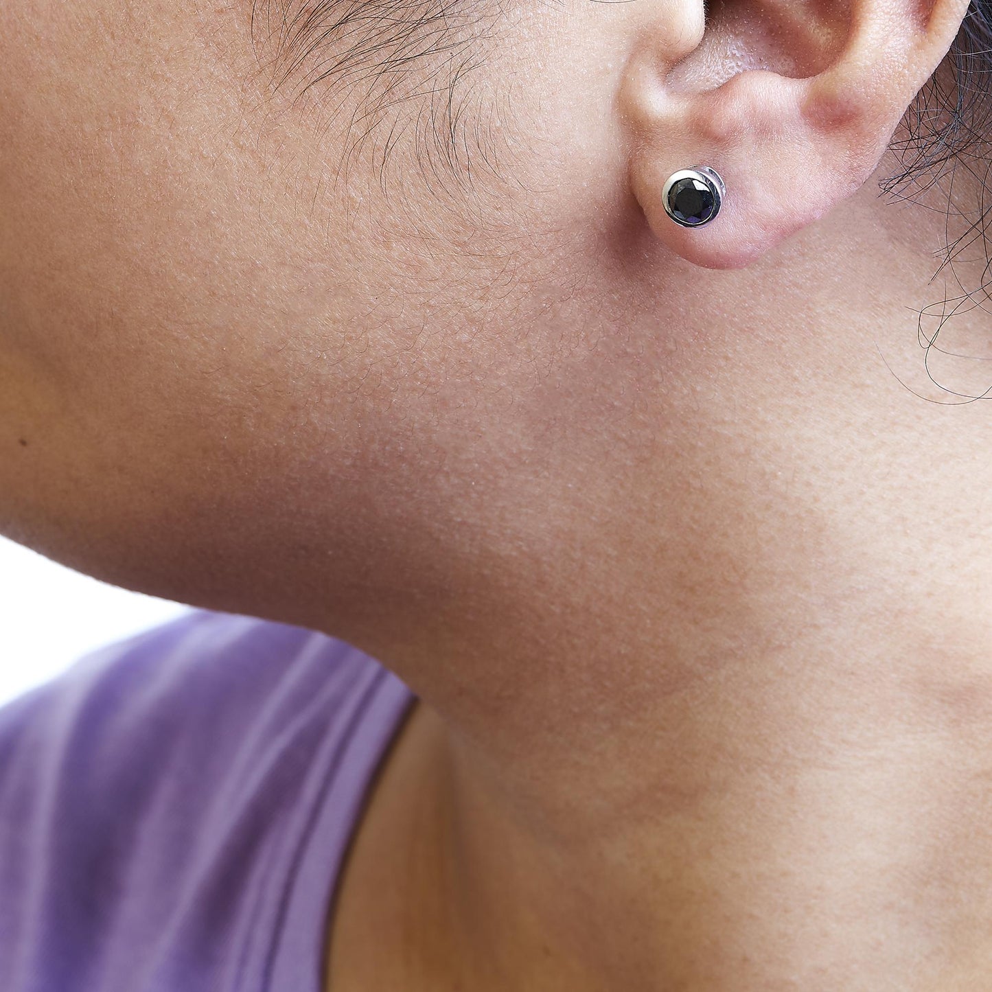 Close-up side angle of a white metal stud earring with a round black gemstone in a bezel setting, worn on a model's ear.