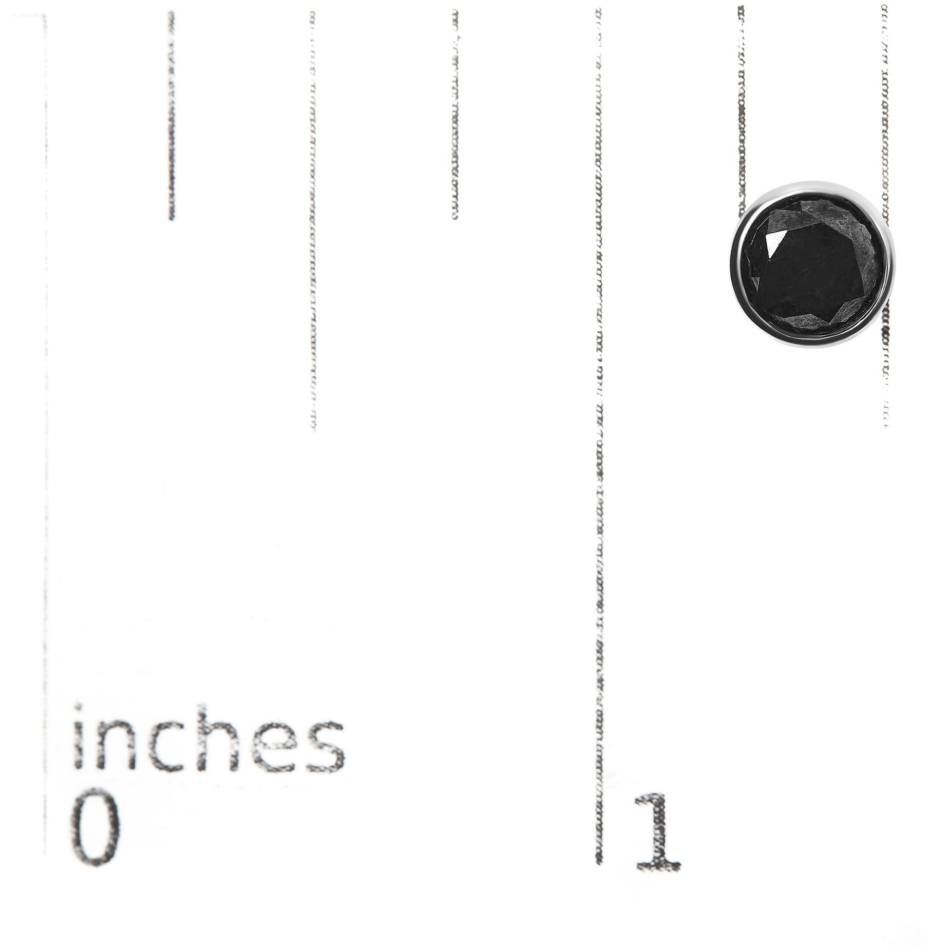 Close-up top view of a single white earring with a round black gemstone in bezel setting, placed on a ruler for size reference.