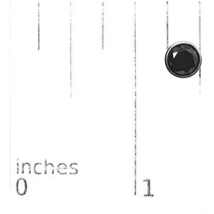 Close-up top view of a single white earring with a round black gemstone in bezel setting, placed on a ruler for size reference.