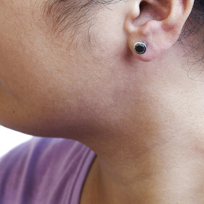 Close-up side view of a white metal stud earring with a round black gemstone in bezel setting worn on a model's ear.