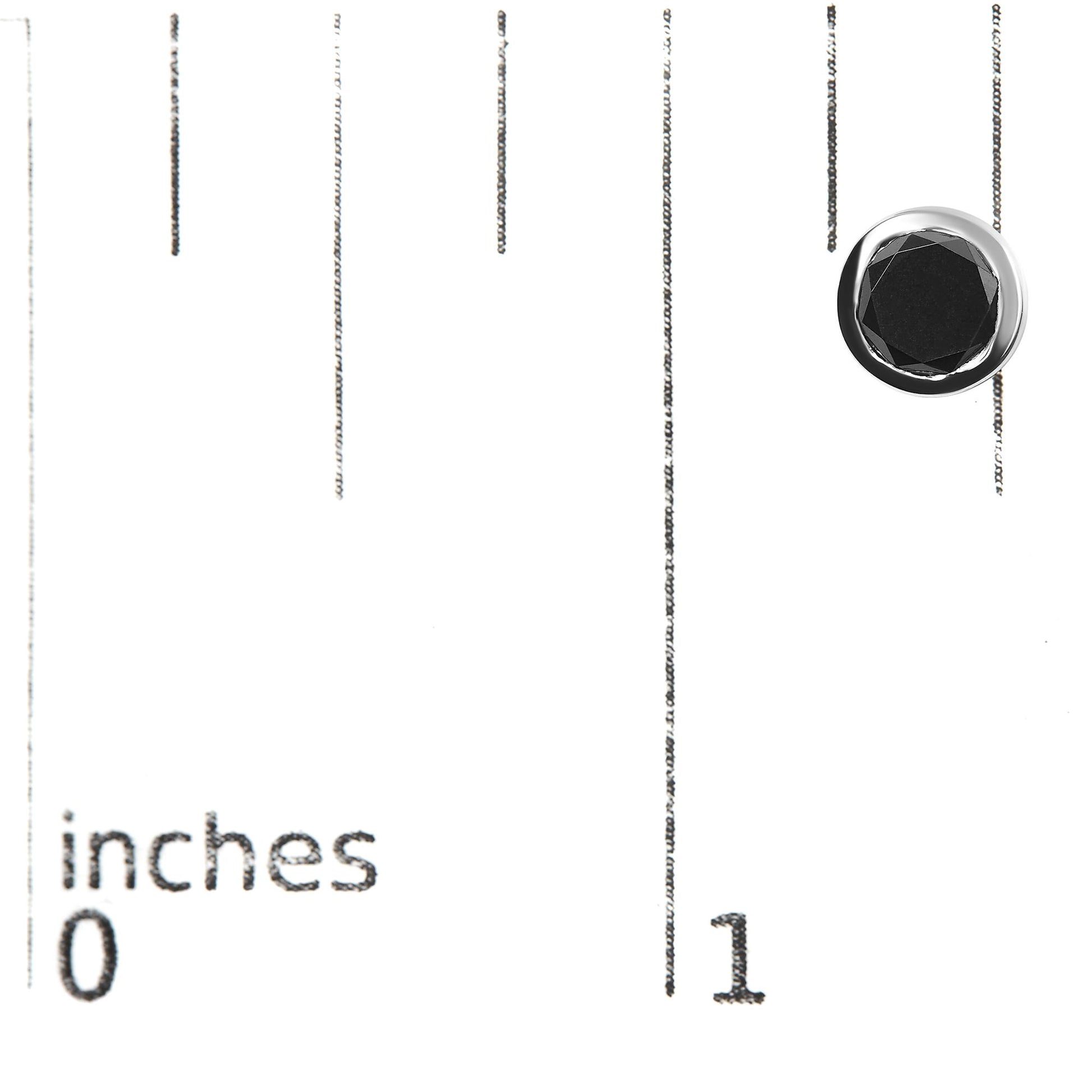 Close-up of a white metal earring with a round black gemstone in bezel setting, placed on a ruler for size reference.
