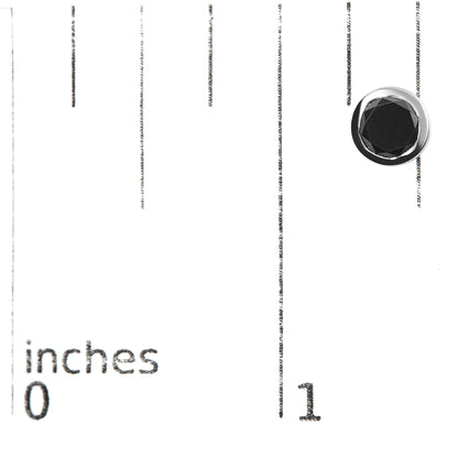 Close-up of a white metal earring with a round black gemstone in bezel setting, placed on a ruler for size reference.