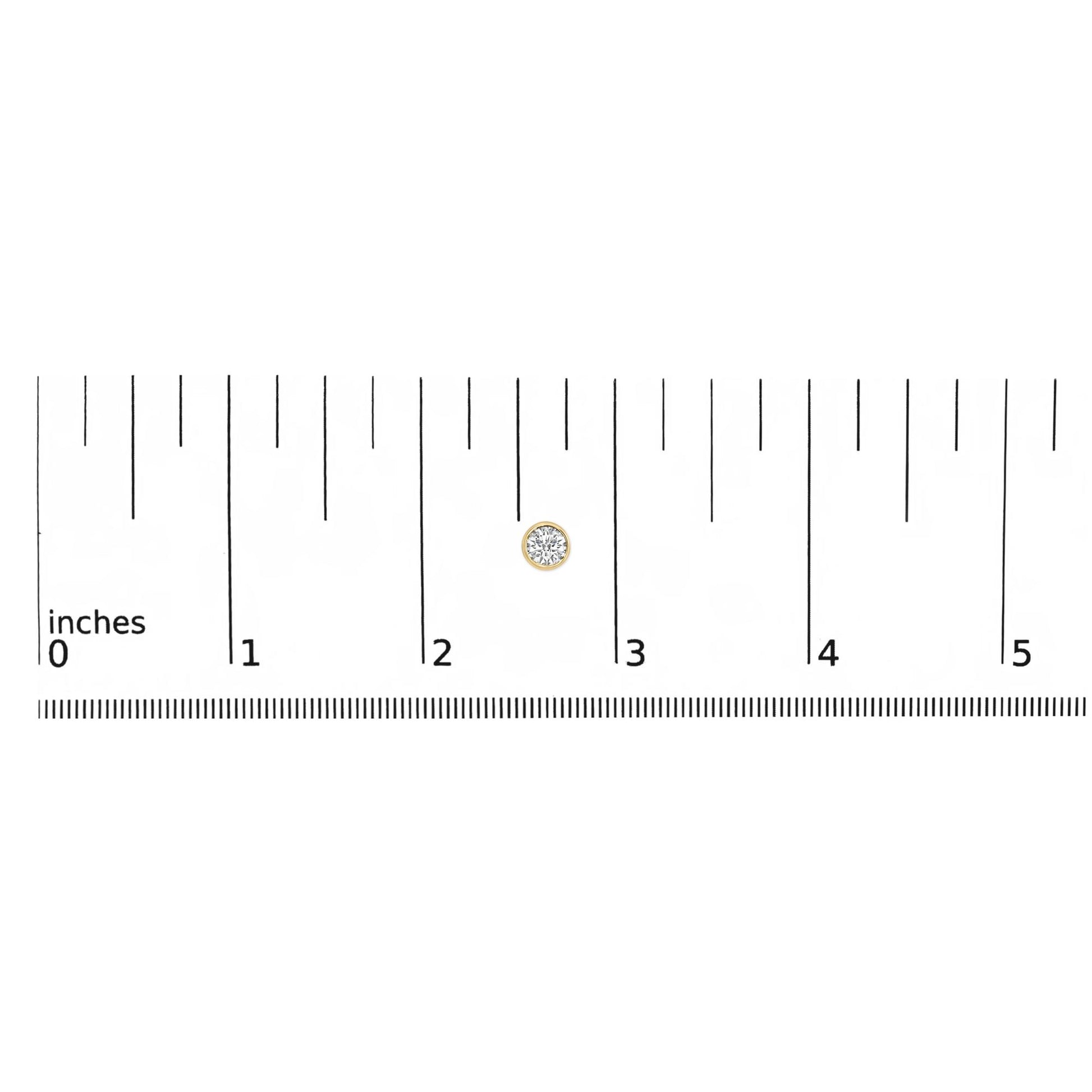 Close-up front view of a yellow metal round bezel-set white gemstone stud earring on a ruler for size reference.
