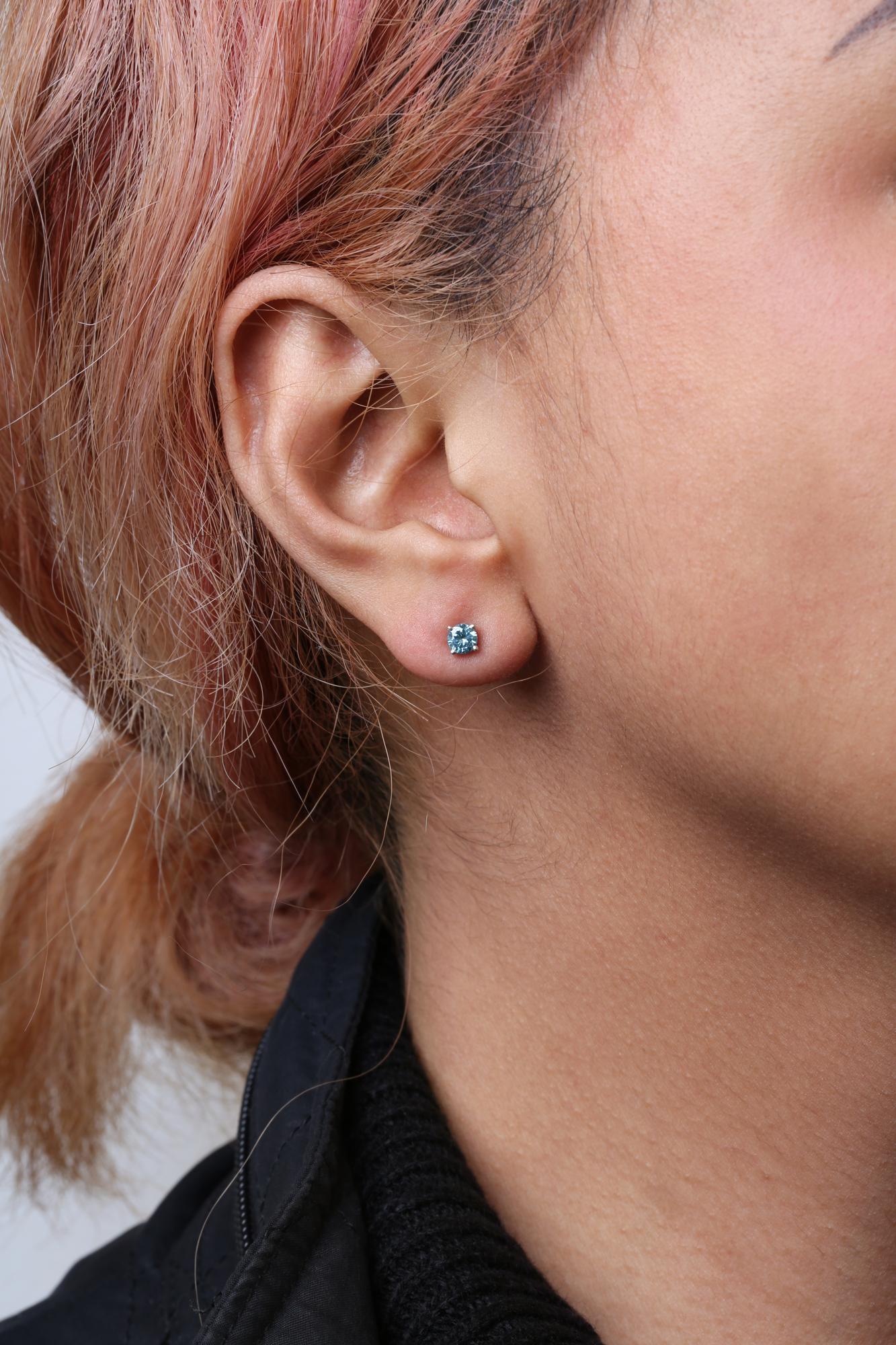 Close-up side view of a white metal stud earring with a round aqua blue gemstone in prong setting, worn on a model.
