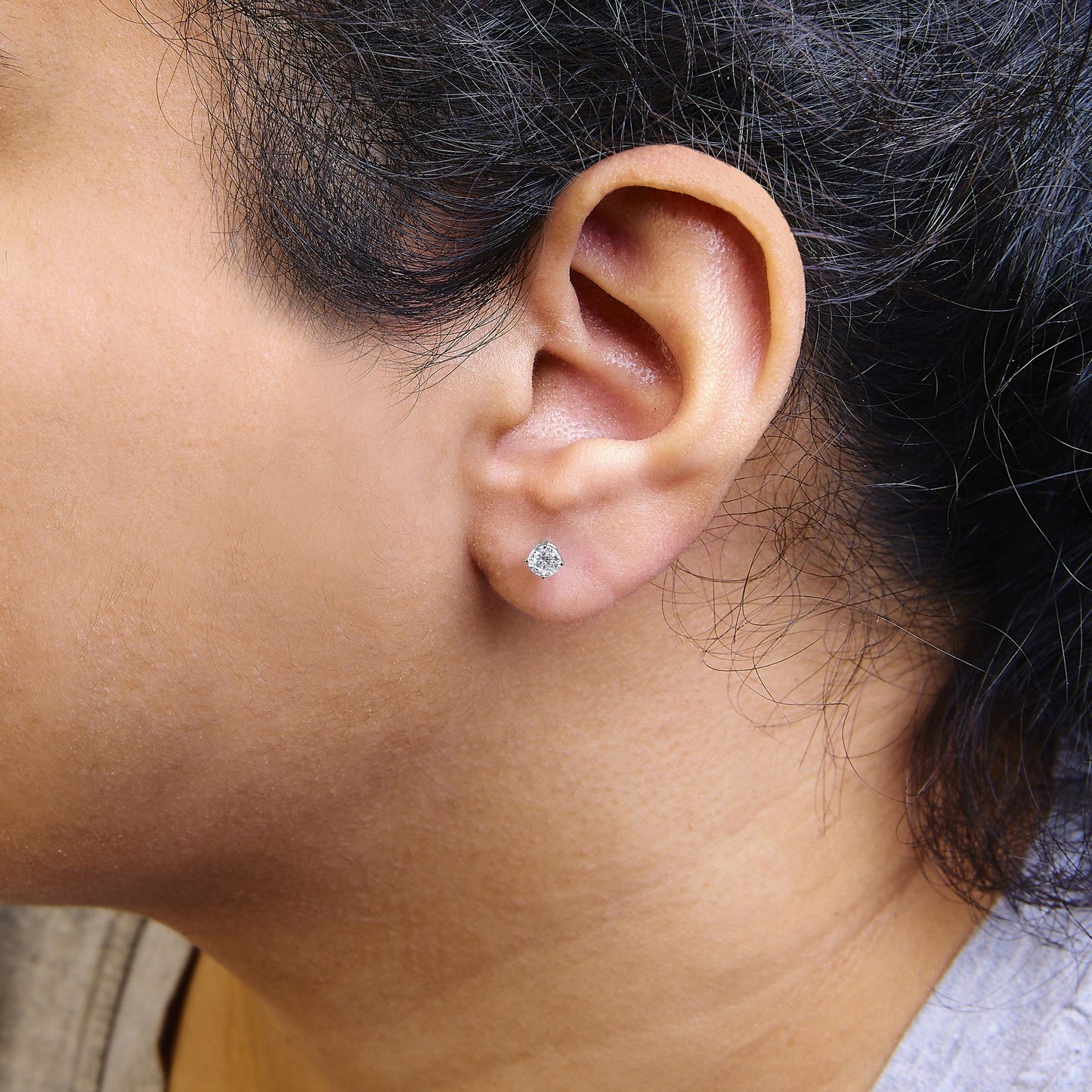 Close-up side view of a model wearing white metal stud earrings with round white gemstones set in four-prong settings.