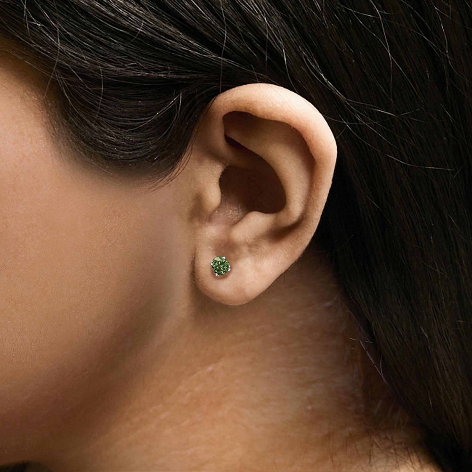 Close-up side view of a white metal earring with a round green gemstone in a 4-prong setting, shown worn on a model's ear.