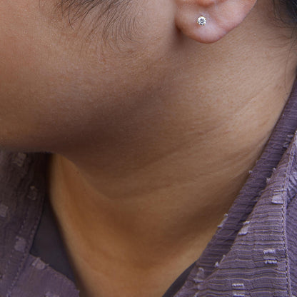Close-up side angle of a model wearing a yellow metal stud earring with a round white gemstone in a 4-prong setting.