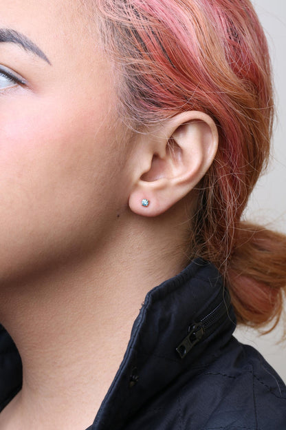 Close-up side view of a model wearing a yellow metal stud earring with a round aqua blue gemstone in prong setting.