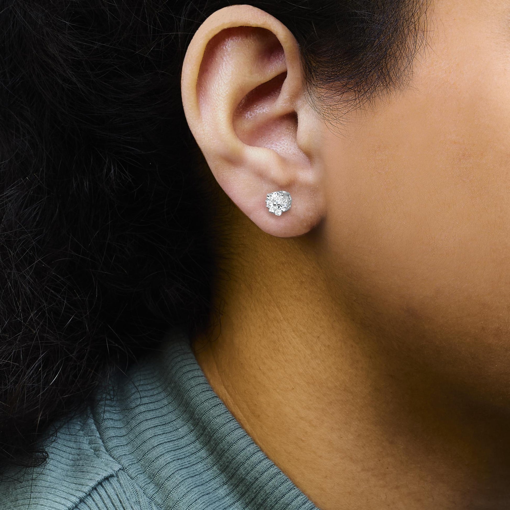 Close-up side view of a model wearing a white metal stud earring with multiple round white gemstones in a prong setting.