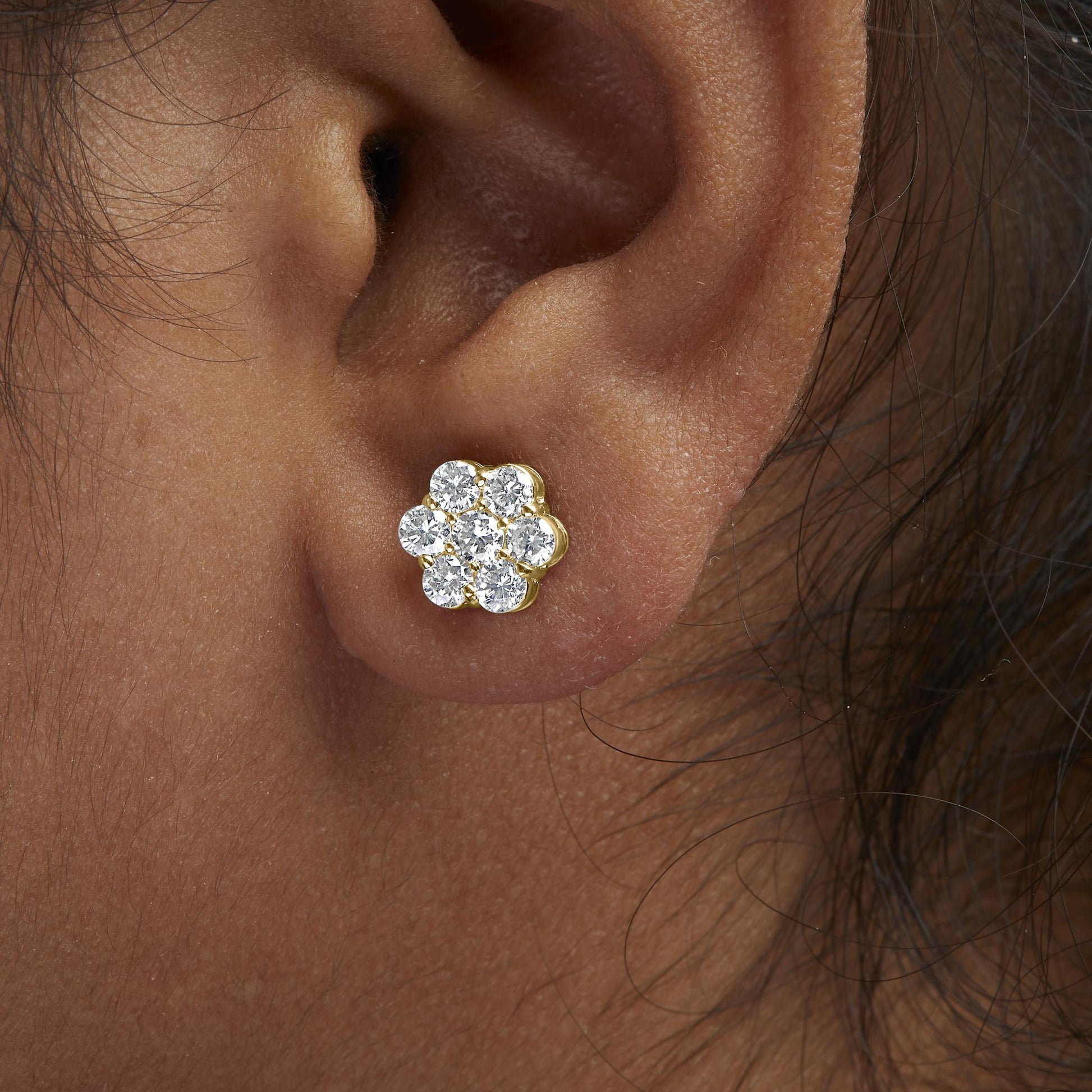 Close-up side view of a yellow metal earring on a model's ear, featuring a cluster of round white gemstones in prong settings.