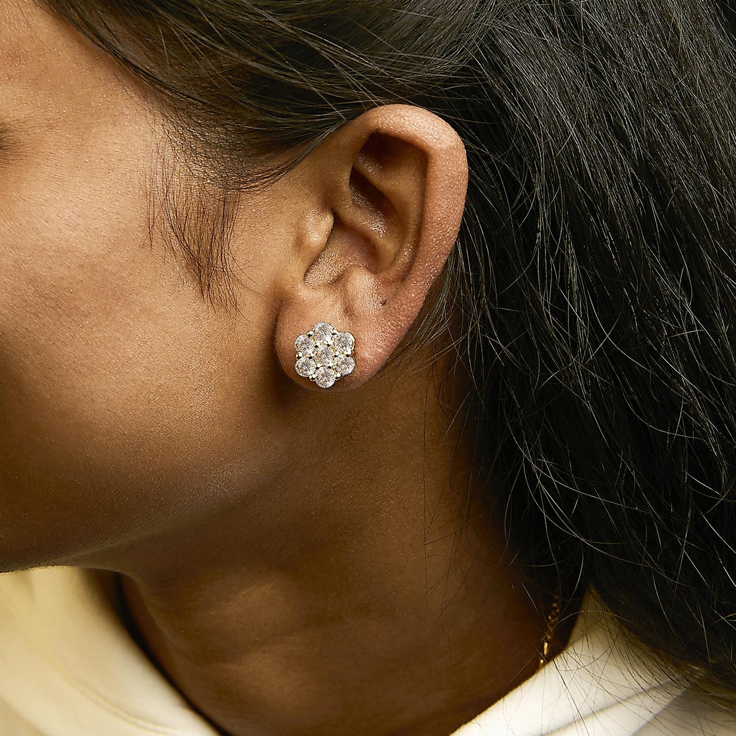Close-up side view of yellow metal cluster earrings with round white gemstones in shared prong setting, shown worn on a model.