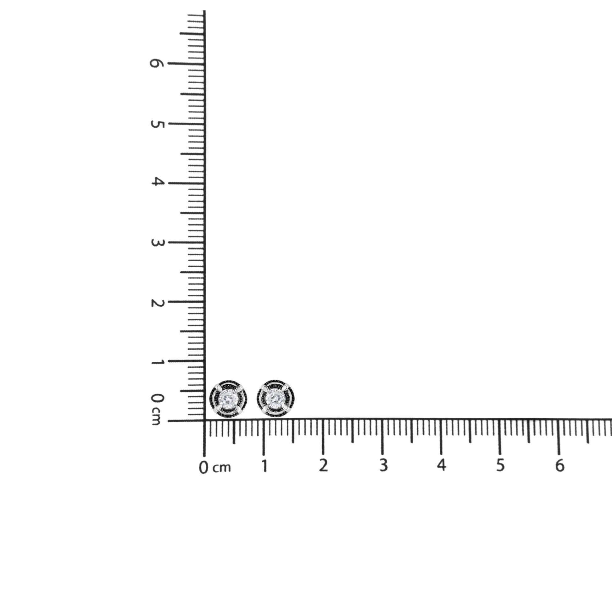 Close-up front view of pair of white metal stud earrings with a round white gemstone in a prong setting shown on a ruler for size reference.