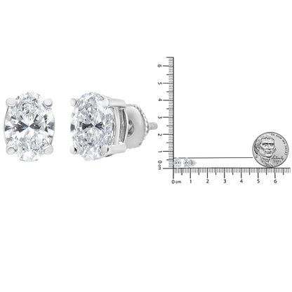 Pair of white metal stud earrings with oval-shaped white gemstones in a 4-prong setting shown at a front and side angle, next to a ruler and coin for size reference.