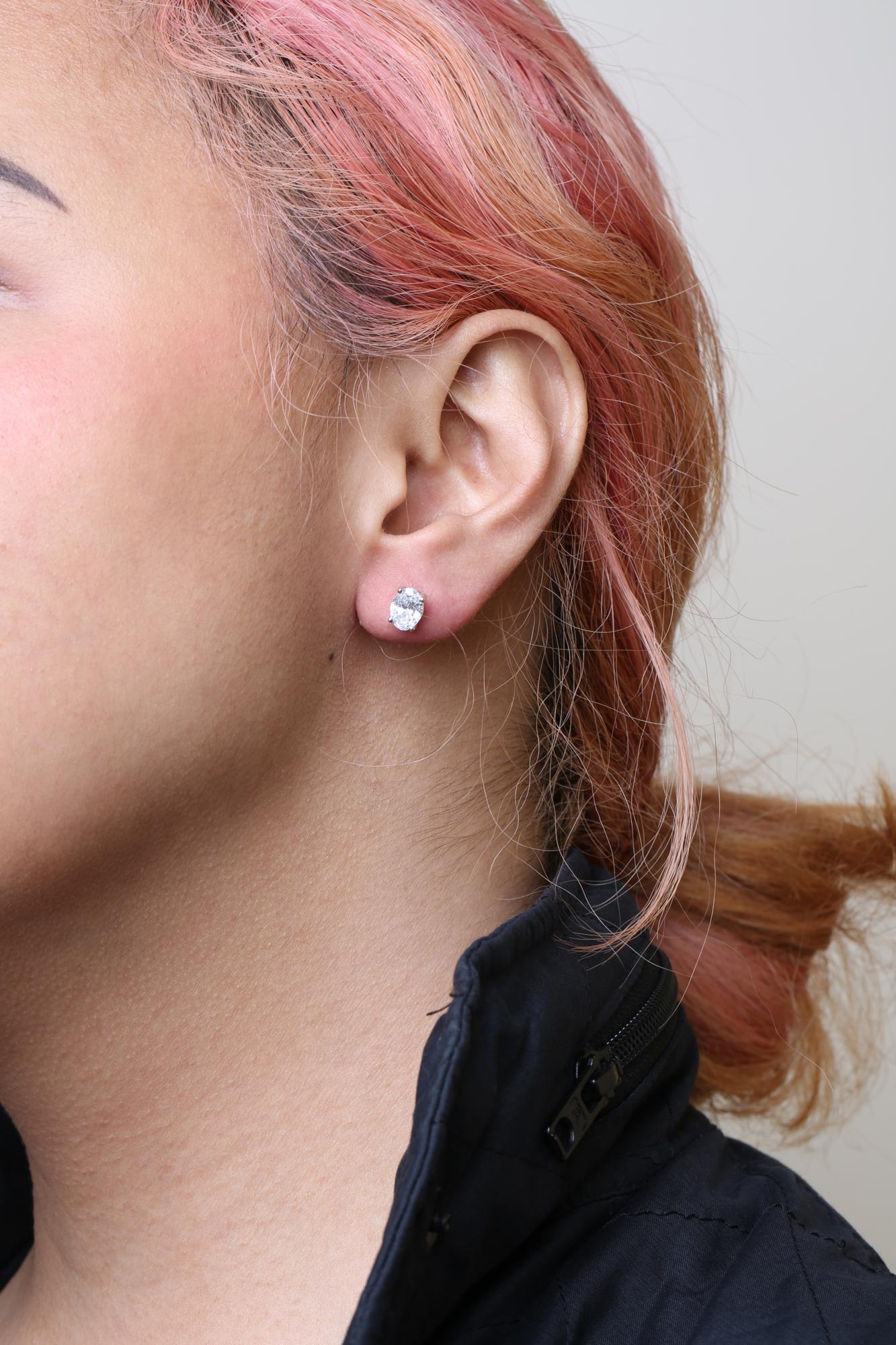 Close-up side view of a white metal stud earring with an oval-shaped white gemstone on a model's ear.