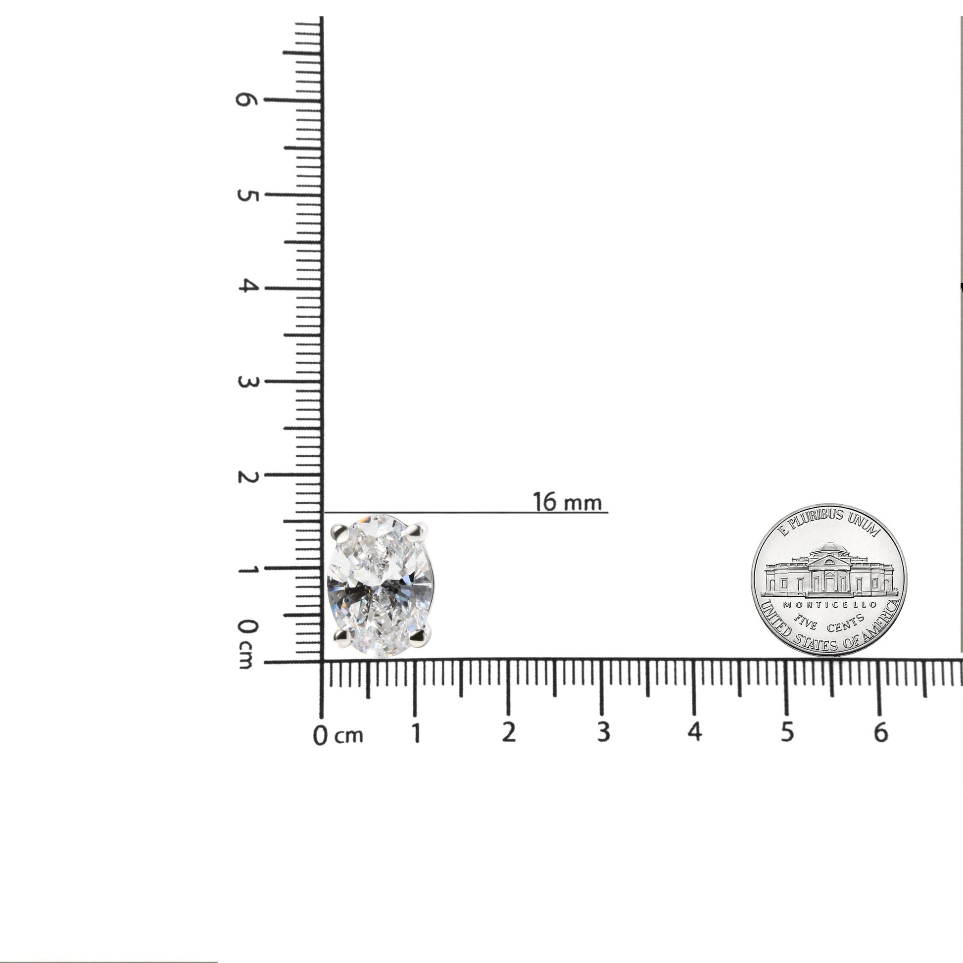 Close-up front view of a white metal earring with an oval-shaped white gemstone in a 4-prong setting, placed on a ruler for size reference.