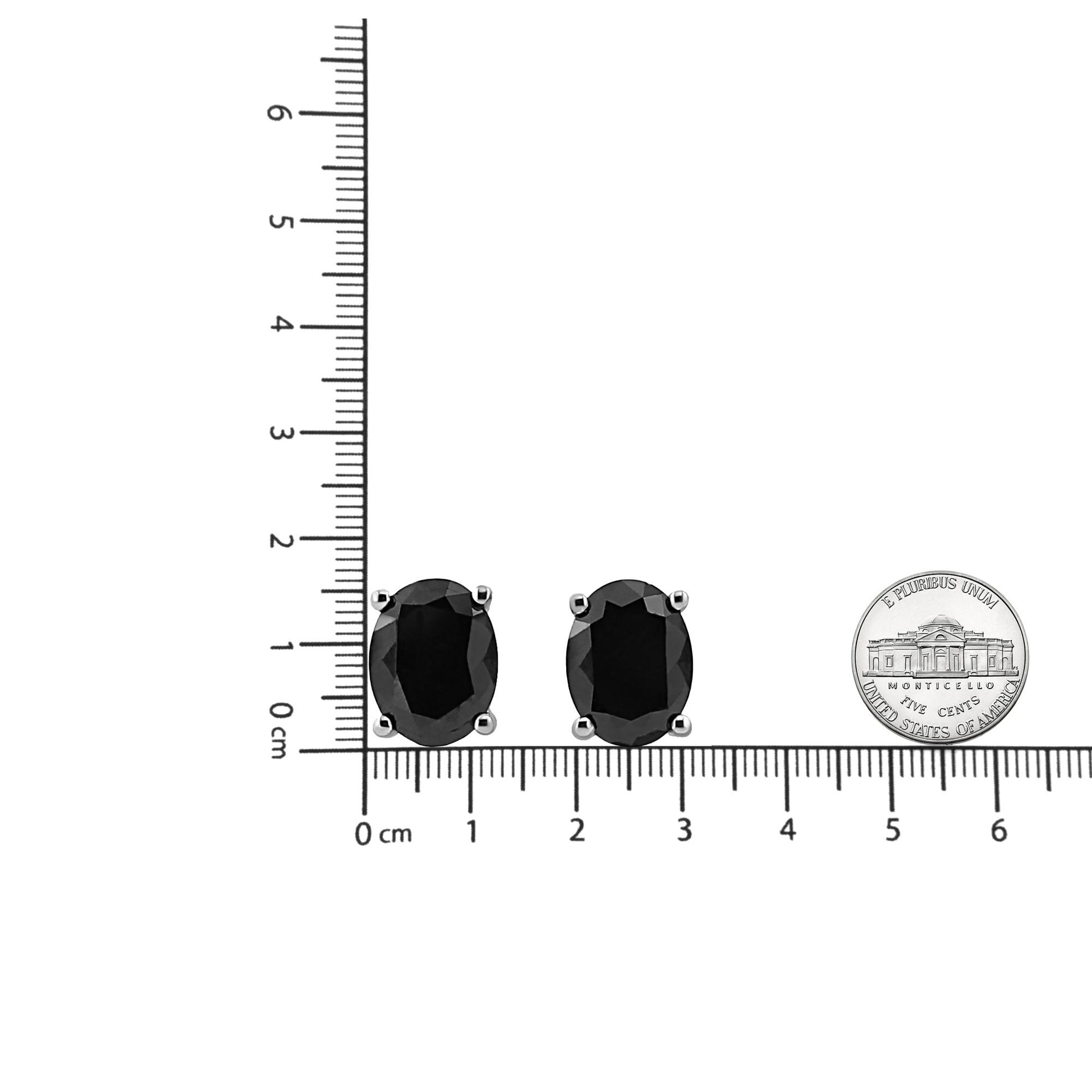 Pair of white metal earrings with oval-shaped black gemstones in prong settings, photographed from the front on a ruler for size reference.