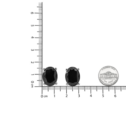 Pair of white metal earrings with oval-shaped black gemstones in prong settings, photographed from the front on a ruler for size reference.