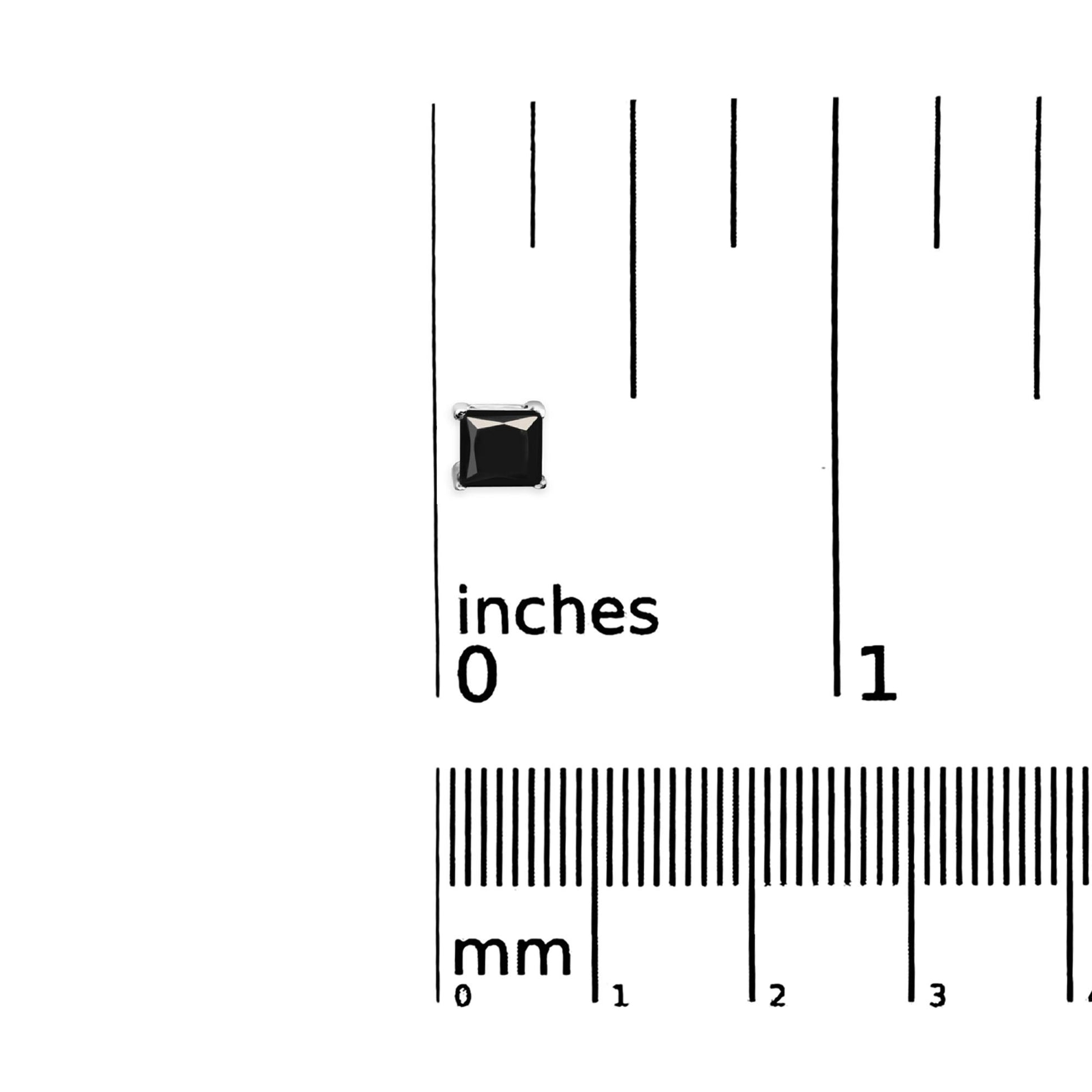 Close-up top view of a white metal earring with a black square-shaped gemstone in prong setting, placed on a ruler for size reference.