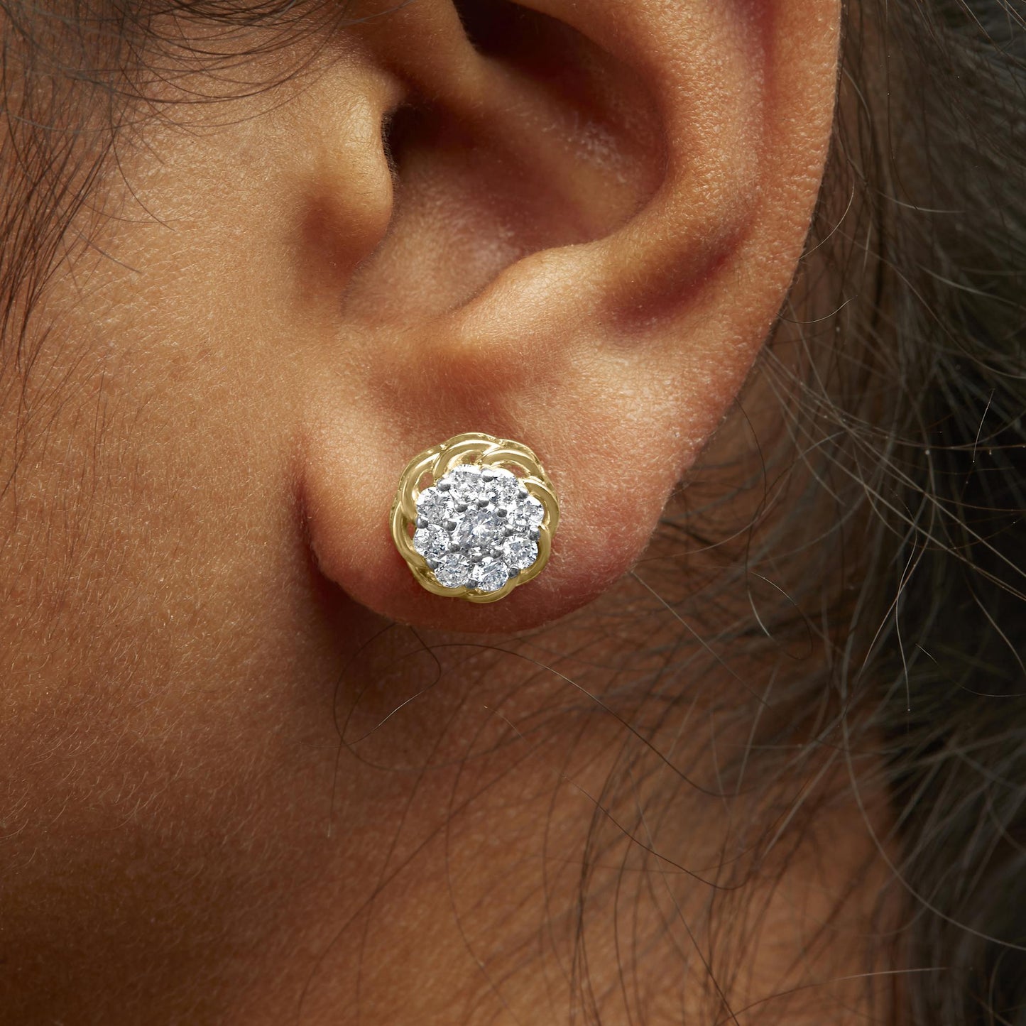 Close-up side angle of a yellow metal earring on a model's ear, featuring a cluster of round white gemstones in prong settings.