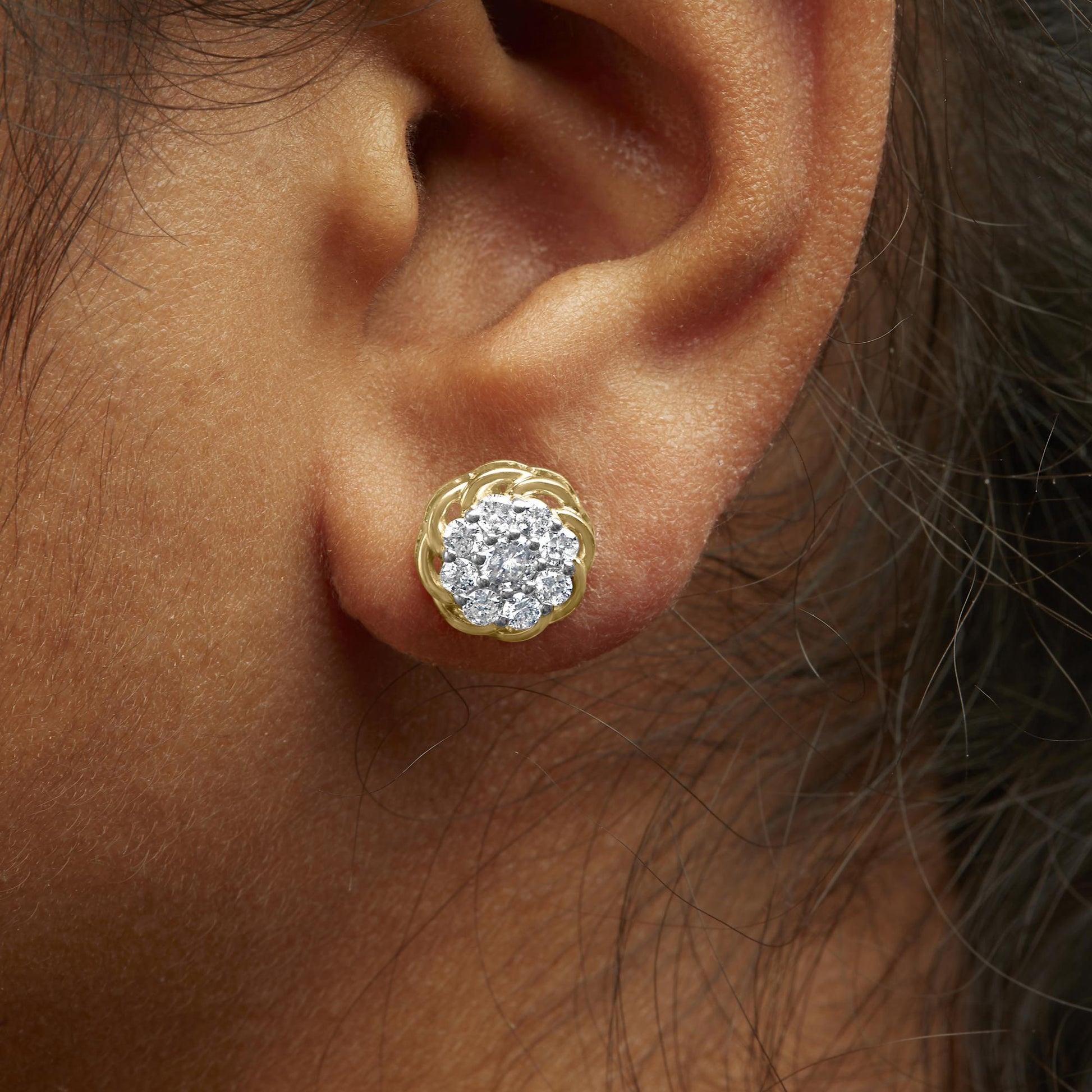 Close-up side angle of a yellow metal earring on a model's ear, featuring a cluster of round white gemstones in prong settings.